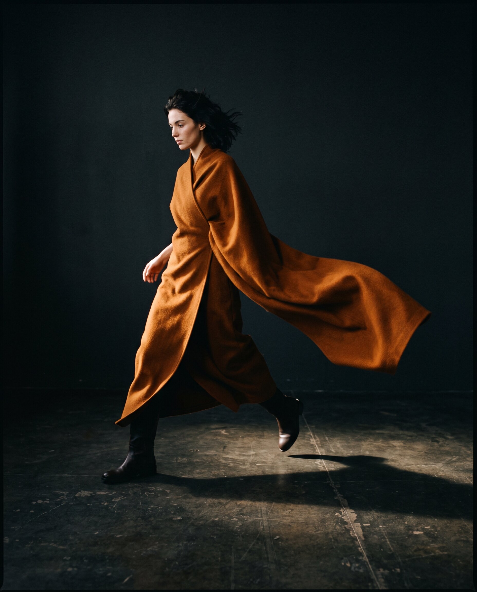Model in draped umber wool, mid-stride, long hard shadow